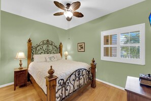 A bedroom with a four-poster bed, two bedside tables with lamps, a ceiling fan, a window with blinds, and a framed picture on the wall. - Vacation In Style At A Great Price!  Bella Lago Deluxe 2B/2B w/ Den Condo Steps From Beach! (Fort Myers Beach)