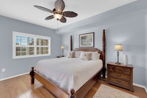 A bedroom with a large bed, a ceiling fan, a window with blinds, a bedside table with a lamp, and a dresser. - Vacation In Style At A Great Price!  Bella Lago Deluxe 2B/2B w/ Den Condo Steps From Beach! (Fort Myers Beach)