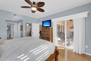 Un dormitorio con cama, ventilador de techo, televisor y puerta corrediza de vidrio que da a un balcón.