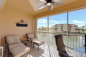 A balcony with two chairs, a ceiling fan, and a view of a building across a body of water. - Vacation In Style At A Great Price!  Bella Lago Deluxe 2B/2B w/ Den Condo Steps From Beach! (Fort Myers Beach)