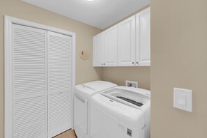 A laundry room with a front-loading washer and dryer, a white closet with louvered doors, and a wall-mounted cabinet above the dryer. - Vacation In Style At A Great Price!  Bella Lago Deluxe 2B/2B w/ Den Condo Steps From Beach! (Fort Myers Beach)