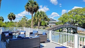 A deck with outdoor furniture, a wooden bridge, and a view of a house and trees.