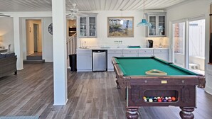 A modern kitchen with a pool table, a dining area, and a view of the outdoors.