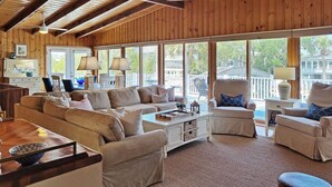 A spacious living room with a high ceiling and wooden beams, featuring a large sofa, armchairs, and a coffee table.