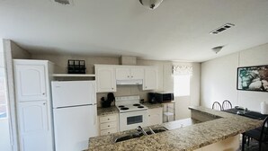 A kitchen with white cabinets, a granite countertop, a refrigerator, a stove, and a microwave.