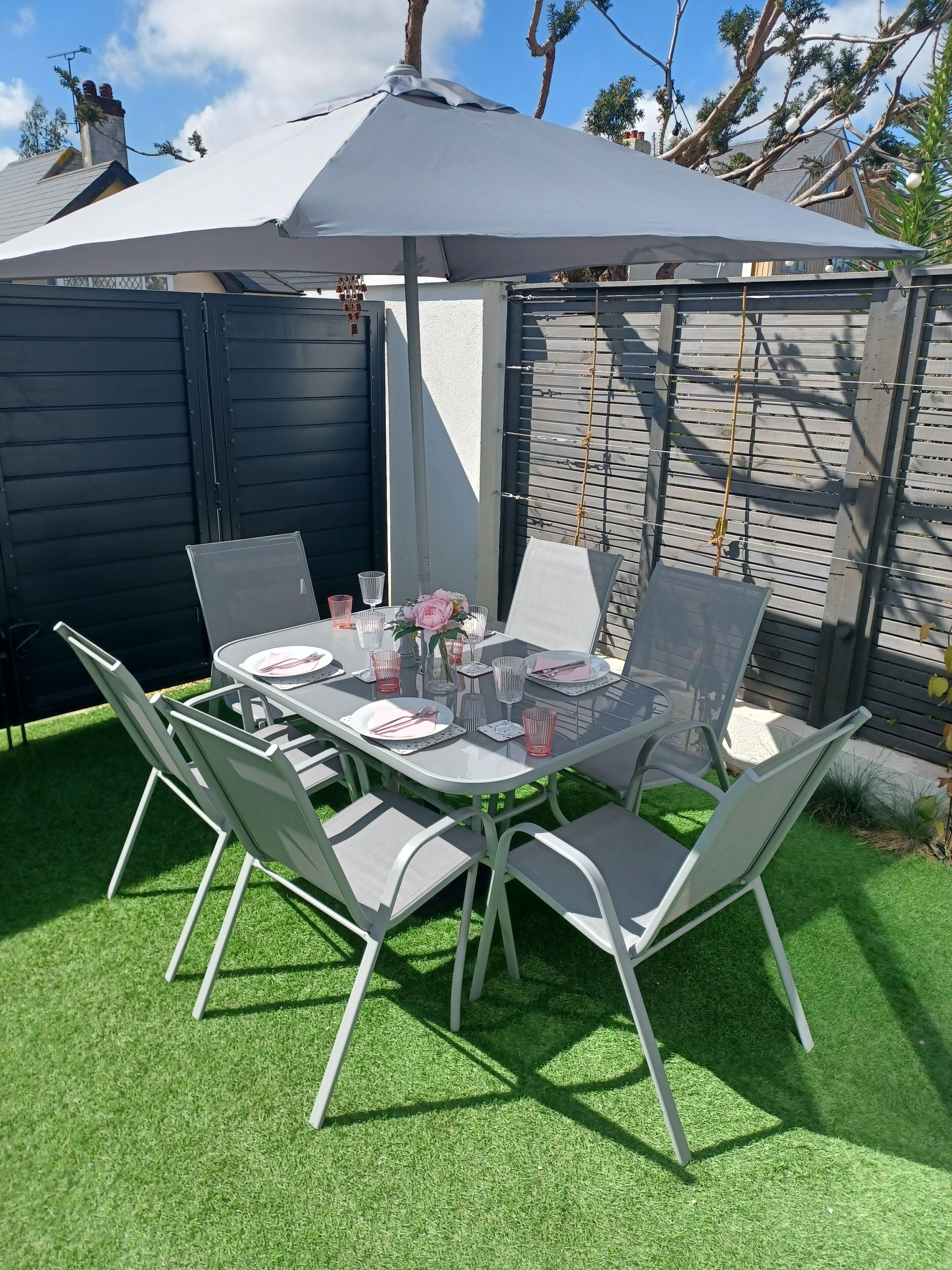 A patio with a table set for four, surrounded by chairs, under a large umbrella.