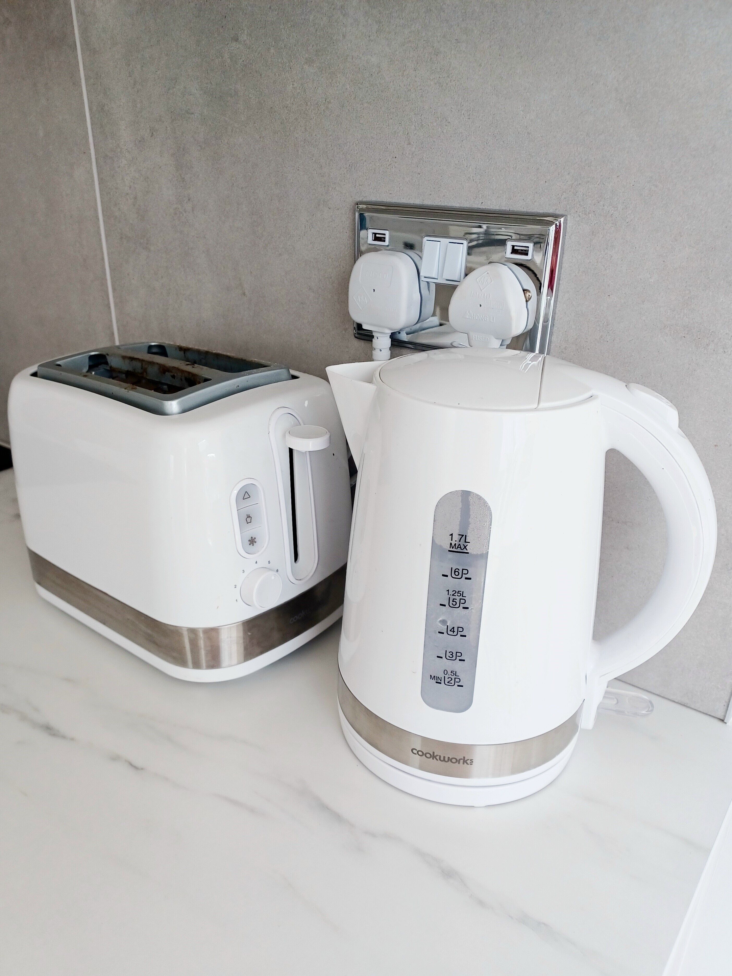A kitchen with a white toaster and a white electric kettle on a marble countertop.