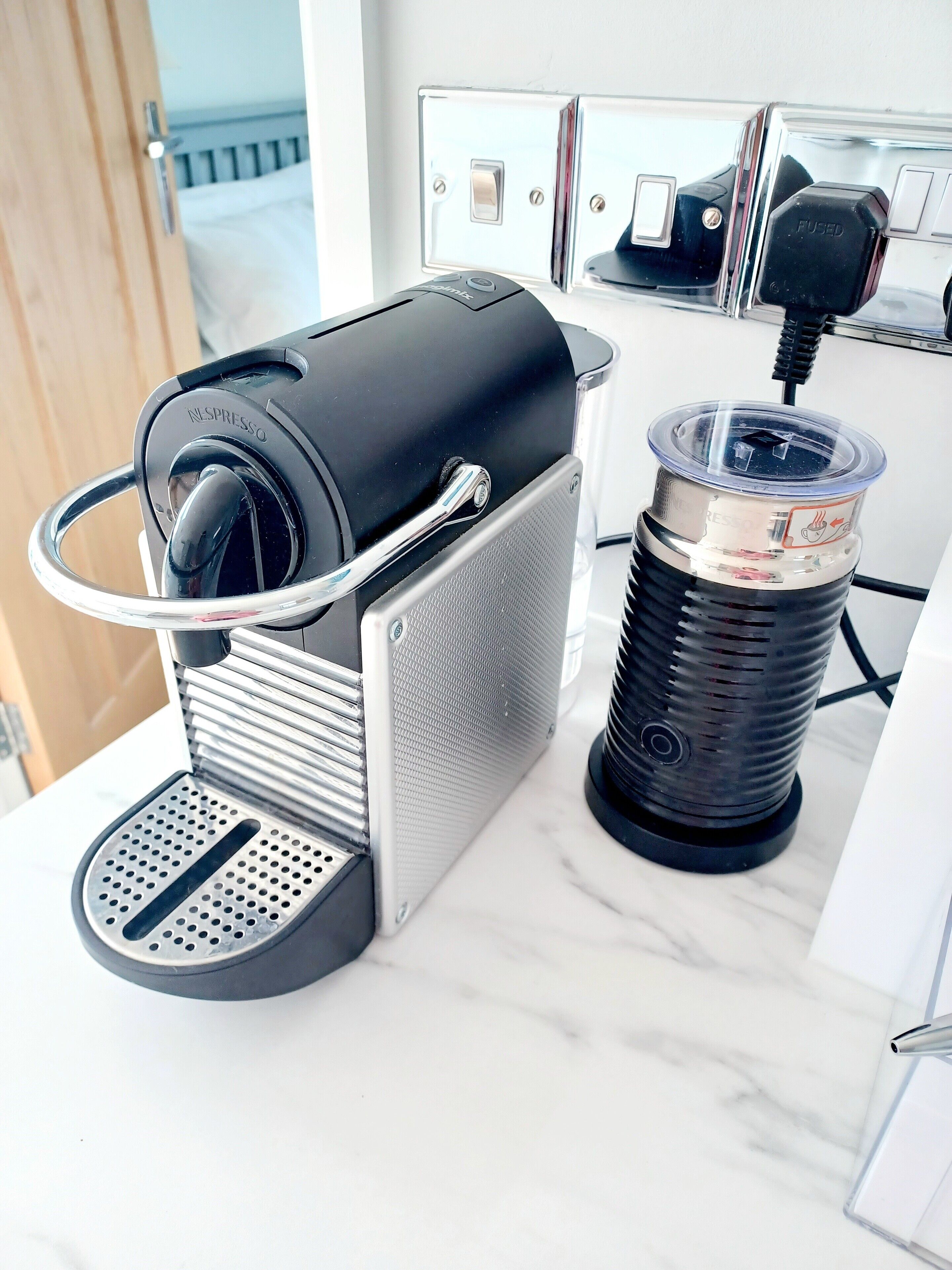 Una macchina per caffè Nespresso con serbatoio dell'acqua e portapod sul piano di un tavolo in marmo.