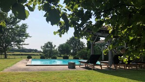Uima-allas, jossa on aurinkotuoleja, pergola ja nurmialue, jossa on puita.
