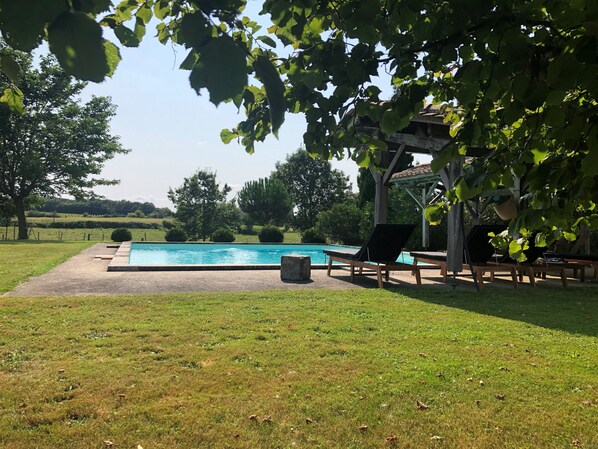 A swimming pool with lounge chairs, a pergola, and a grassy area with trees.