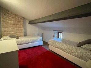 A small, cozy attic bedroom with two single beds, a red carpet, and a stone wall.
