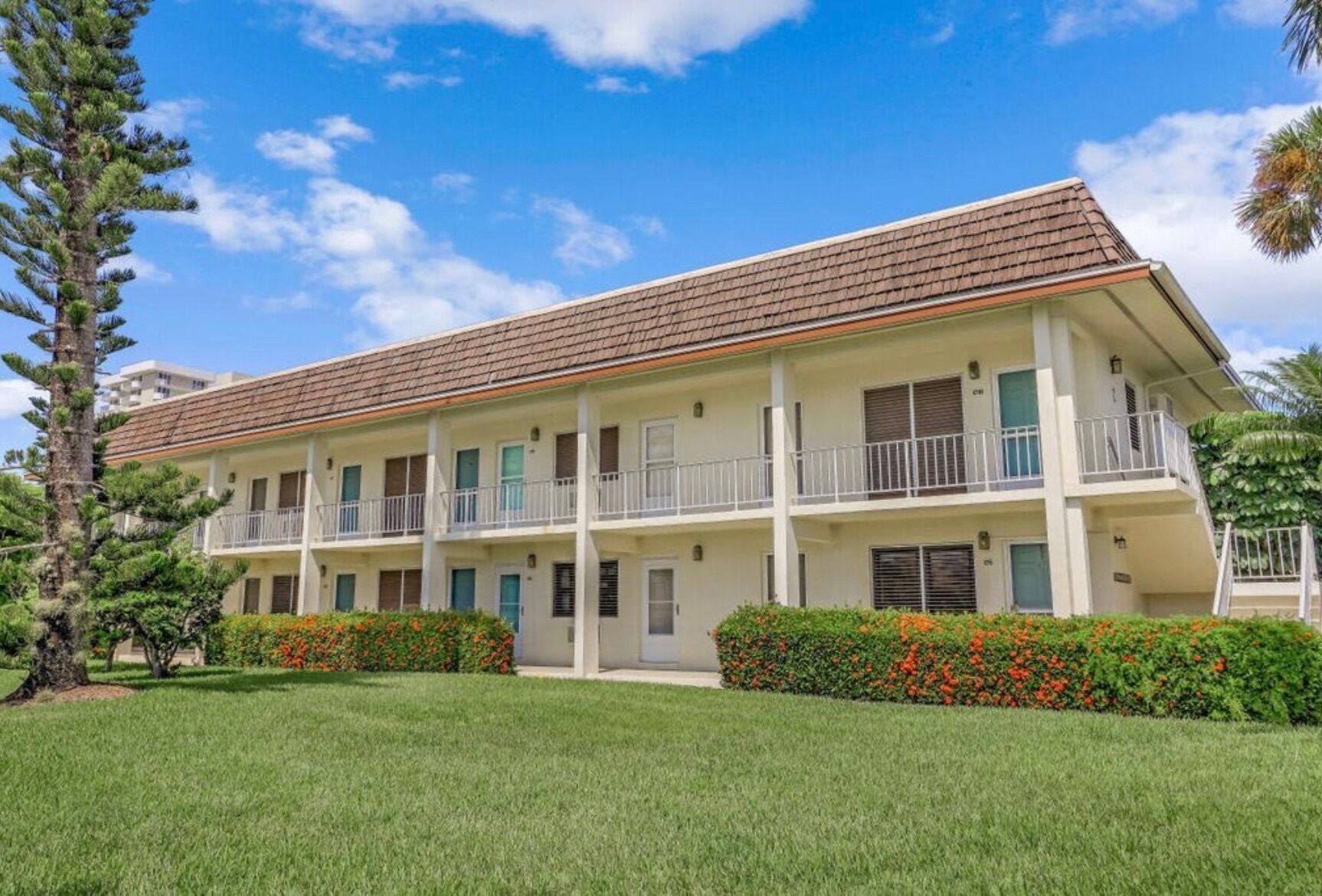 A multi-story hotel with a flat roof, balconies, and a well-maintained lawn.