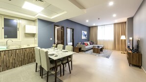 Una habitación de hotel moderna con zona de comedor, sofá, televisor y baño.