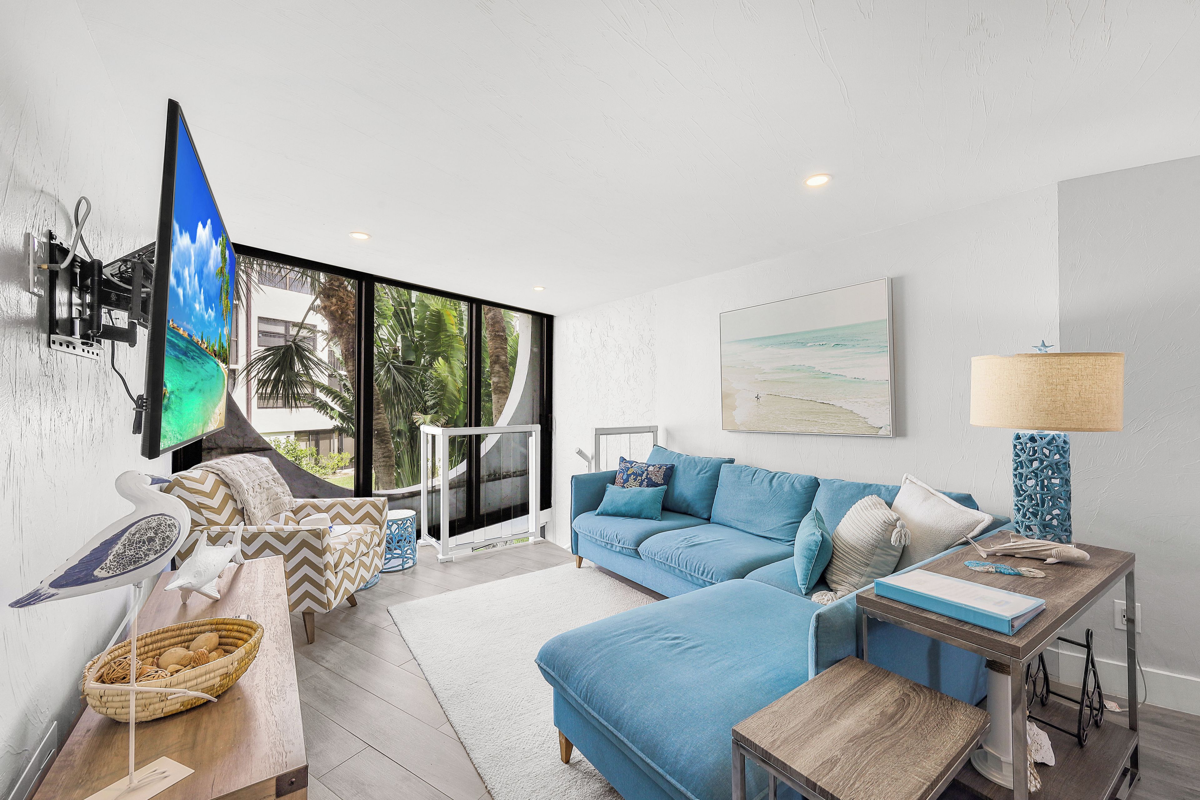 A modern living room with a large TV, a blue sofa, a wooden coffee table, and a view of the outdoors.