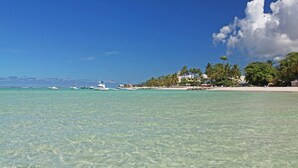 Una playa con agua turquesa cristalina, barcos y una hilera de palmeras y edificios a lo largo de la orilla.