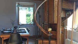 A wooden dining area with a table set for four, a black chair, and a staircase with a wooden railing and a brass baluster.