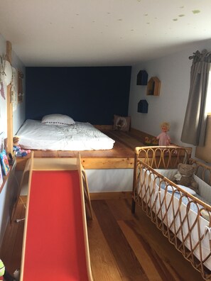 A child's room with a bunk bed, a small wooden crib, and a red play mat.
