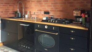 A kitchen with a brick backsplash, black cabinetry, a wooden countertop, a built-in oven, and a black range hood.
