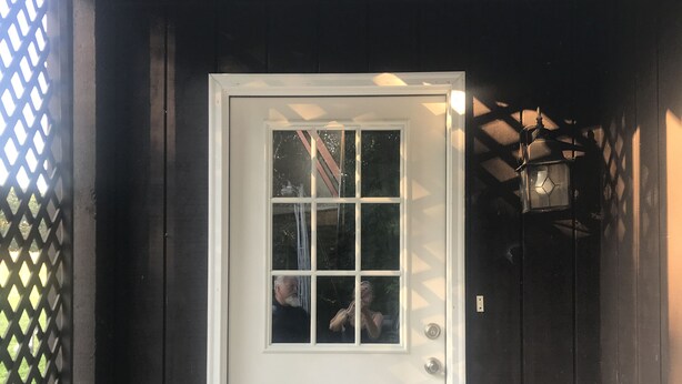 Eine weiße Tür mit Fenster, einer Fußmatte und ein kleiner weißer Tisch mit einer Laterne daneben.