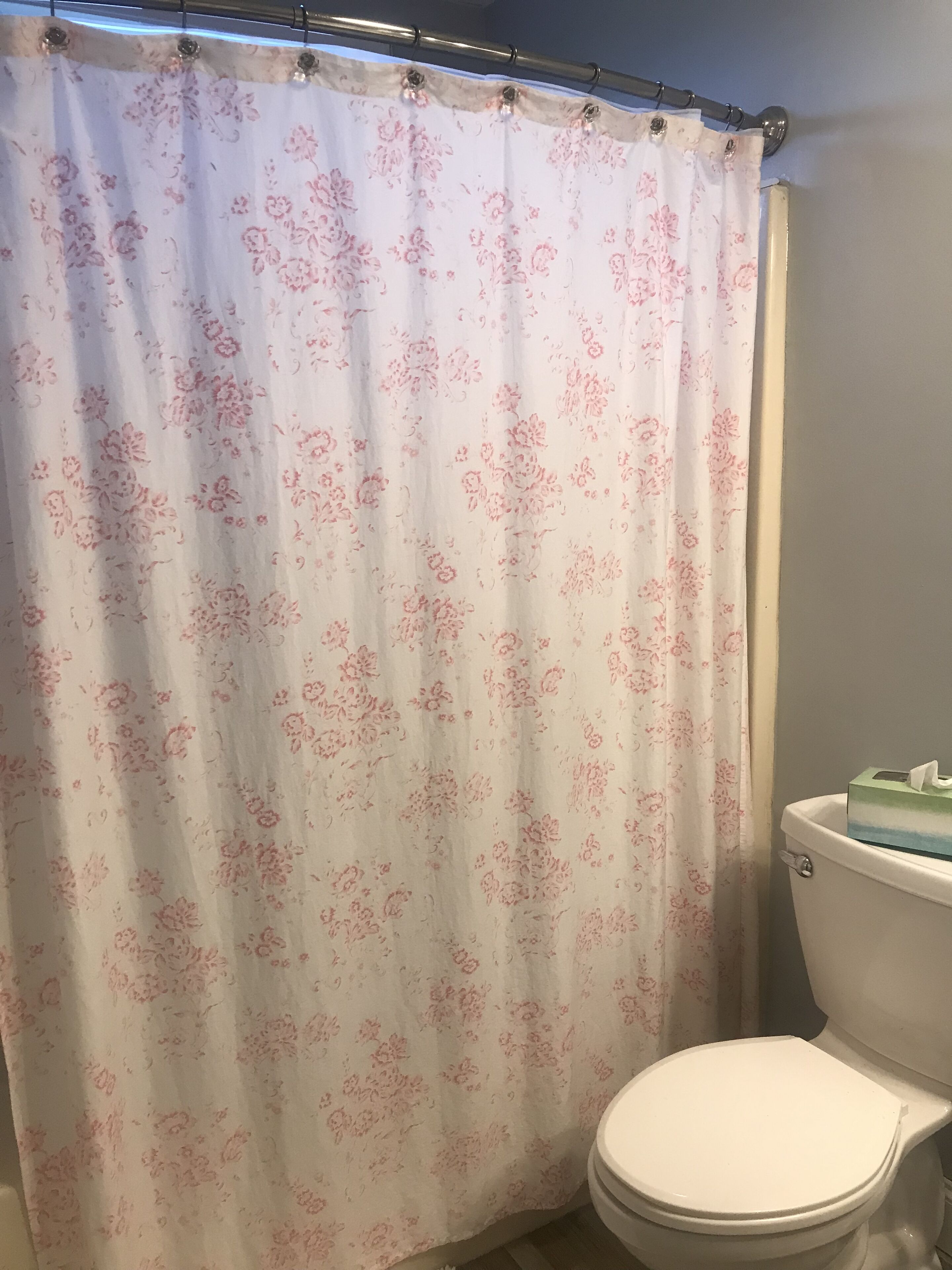 A bathroom with a floral shower curtain, a white toilet, and a tissue box on the toilet tank.