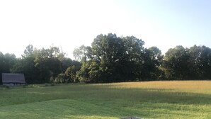 Eine Holzterrasse mit einem Metalltisch und zwei Stühlen, mit Blick auf eine Wiese und Bäume.