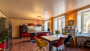 Une cuisine moderne avec un plancher en bois, un coin repas avec des chaises rouges et jaunes, et une grande fenêtre donnant sur l’extérieur.