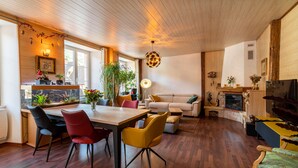 Un salon spacieux avec un plafond en bois, un coin repas doté de chaises modernes, un canapé et une cheminée.