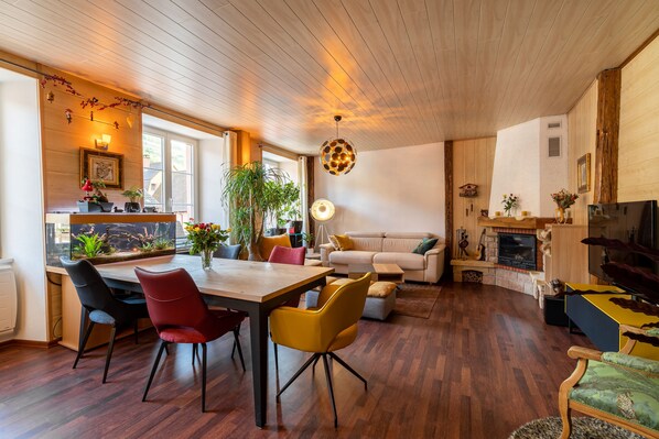 A spacious living room with a wooden ceiling, a dining area with modern chairs, a sofa, and a fireplace.