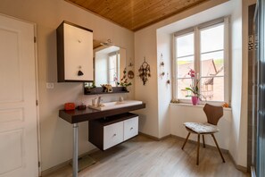 Un baño moderno con techo de madera, un espejo grande, un lavamanos integrado y una ventana con vista a un edificio.