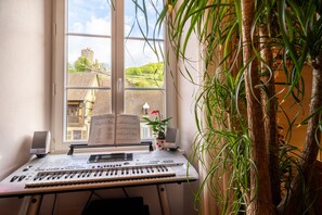 Ein Zimmer mit einem Klavier, Lautsprechern und einem Fenster mit Blick auf ein Gebäude.