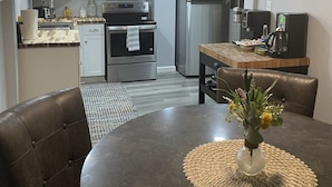 Una cocina moderna con armarios blancos, electrodomésticos de acero inoxidable y un comedor con mesa redonda y sillas.