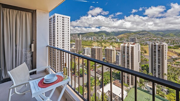 Ein Balkon mit Blick auf eine Stadtlandschaft, einschließlich Hochhäusern und Bergen.