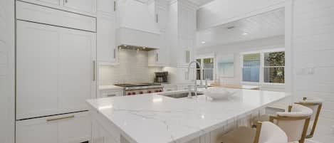 A modern kitchen with white cabinetry, a large island with seating, and a view to the outside.