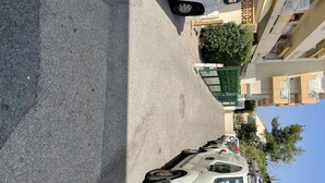 Parkkialue, jossa on useita autoja, valkoinen pakettiauto sekä parvekkeilla varustettu rakennus ja portilla suljettu sisäänkäynti.