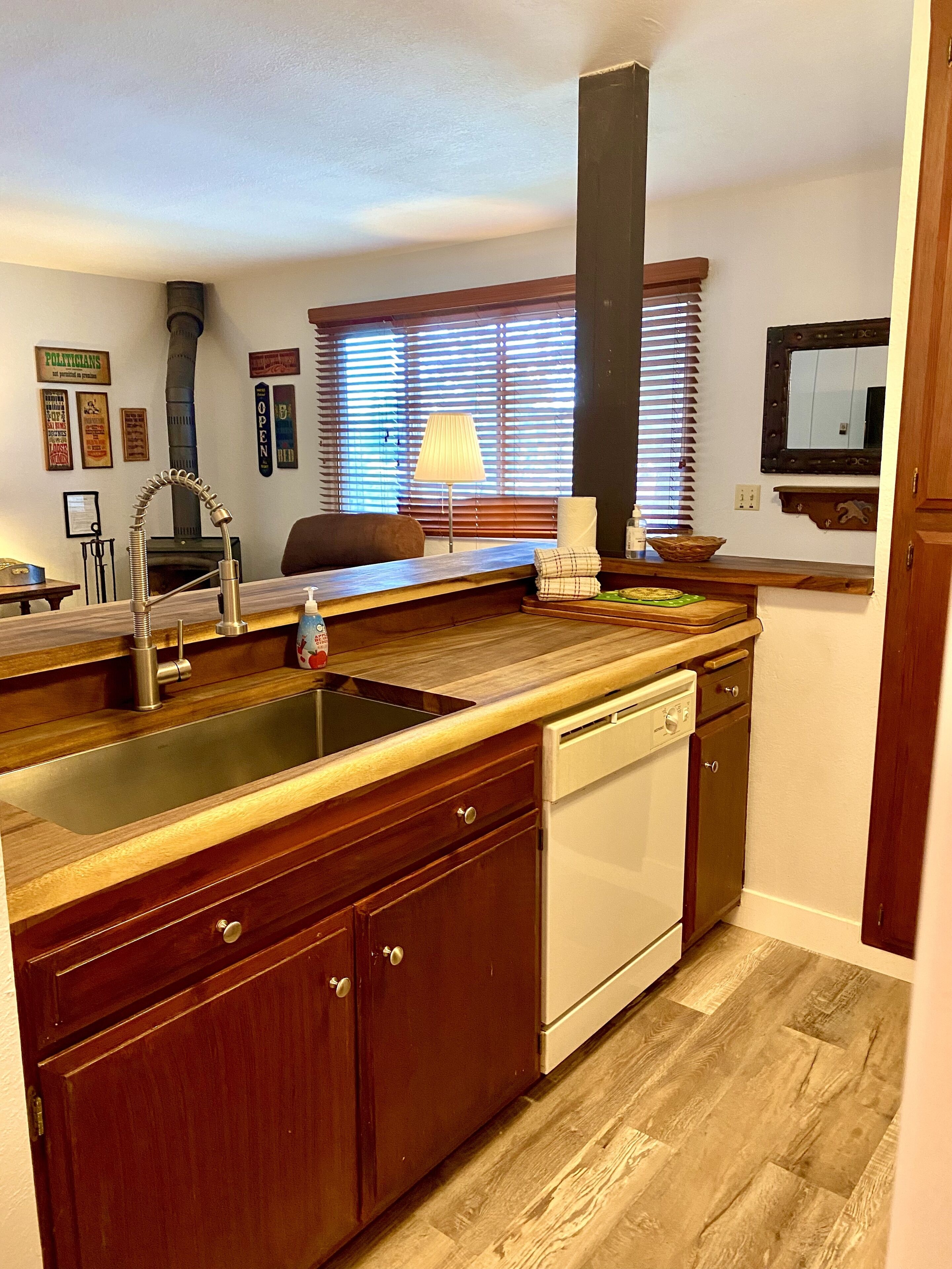 A kitchen with wooden cabinets, a built-in dishwasher, and a window with blinds.