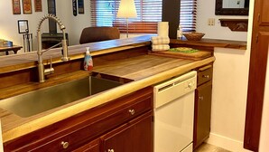 Een keuken met houten kastjes, een inbouwvaatwasser en een raam met zonwering.