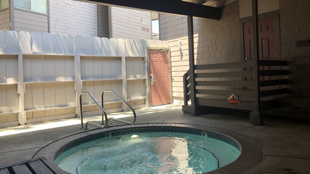 Een hottub met een houten terras en metalen leuning, omringd door een bakstenen muur en een overdekt gedeelte met een deur.