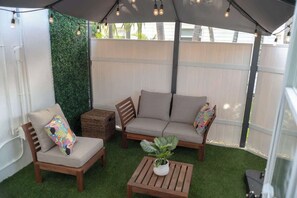 Un área de estar al aire libre con sofá, sillas y una mesa bajo un toldo.
