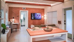 A modern living room with a wooden coffee table, a flat-screen TV mounted on the wall, a sofa, and a dining area with a table set for two.