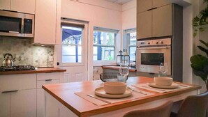 A modern kitchen with white cabinets, a wooden countertop, a gas stove, an oven, and a dining area with a table set for two.