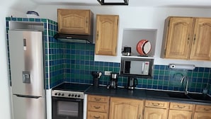A compact kitchen with a stainless steel refrigerator, a stove, a microwave, wooden cabinets, and a tiled backsplash. - Au 10 fontaines (Etoges)