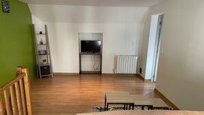 A spacious living area with a wooden floor, a television on a stand, a radiator, and a green wall. - Au 10 fontaines (Etoges)