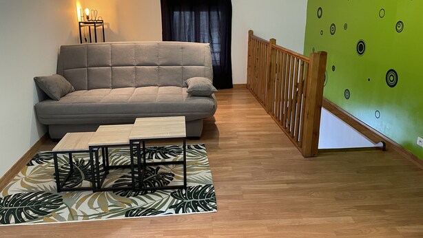 A living room with a grey sofa, a wooden coffee table, a patterned rug, and a green wall with circular designs. - Au 10 fontaines (Etoges)
