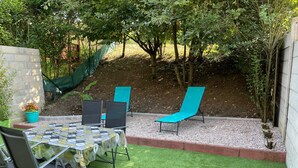 A patio with a table and chairs, surrounded by a garden with trees and a gravel path. - Au 10 fontaines (Etoges)