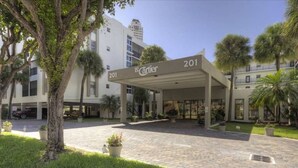 A hotel entrance with a covered walkway, palm trees, and a building in the background. - Le Cartier 207 STR-02440 (Sunny Isles Beach)