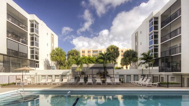 A swimming pool with lounge chairs and a view of a multi-story building with balconies. - Le Cartier 207 STR-02440 (Sunny Isles Beach)