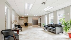 A spacious lobby with a marble floor, a leather sofa, and a table with chairs. - Le Cartier 207 STR-02440 (Sunny Isles Beach)