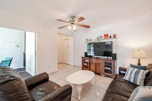 A living room with a ceiling fan, a flat-screen TV, a wooden cabinet, and a sofa.