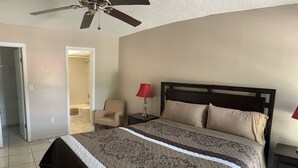 A bedroom with a bed, a chair, a nightstand, a ceiling fan, and a door leading to another room. - Le Cartier 207 STR-02440 (Sunny Isles Beach)