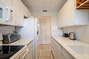 A narrow kitchen with white cabinets, a microwave, a toaster, and a kettle.